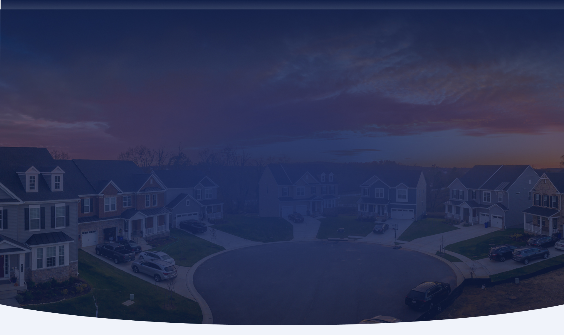 An aerial view of a suburban cul-de-sac lined with new homes under a vivid orange and pink sunset sky.